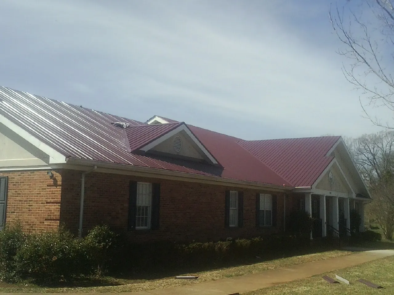 Red metal roof with gabled entries on a long brick building, from a Hail Damage Roof Repair job in Seminole